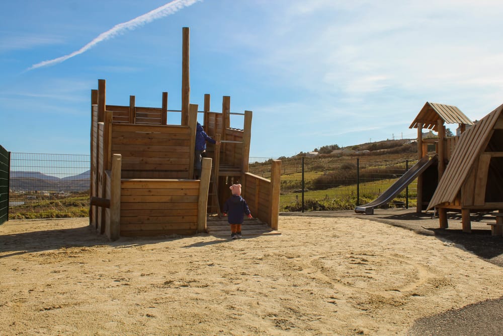 a child standing next to a play structure in a sandy area