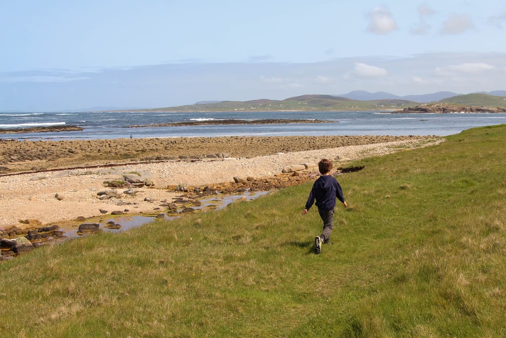 a boy running on a grassy hill near a beach